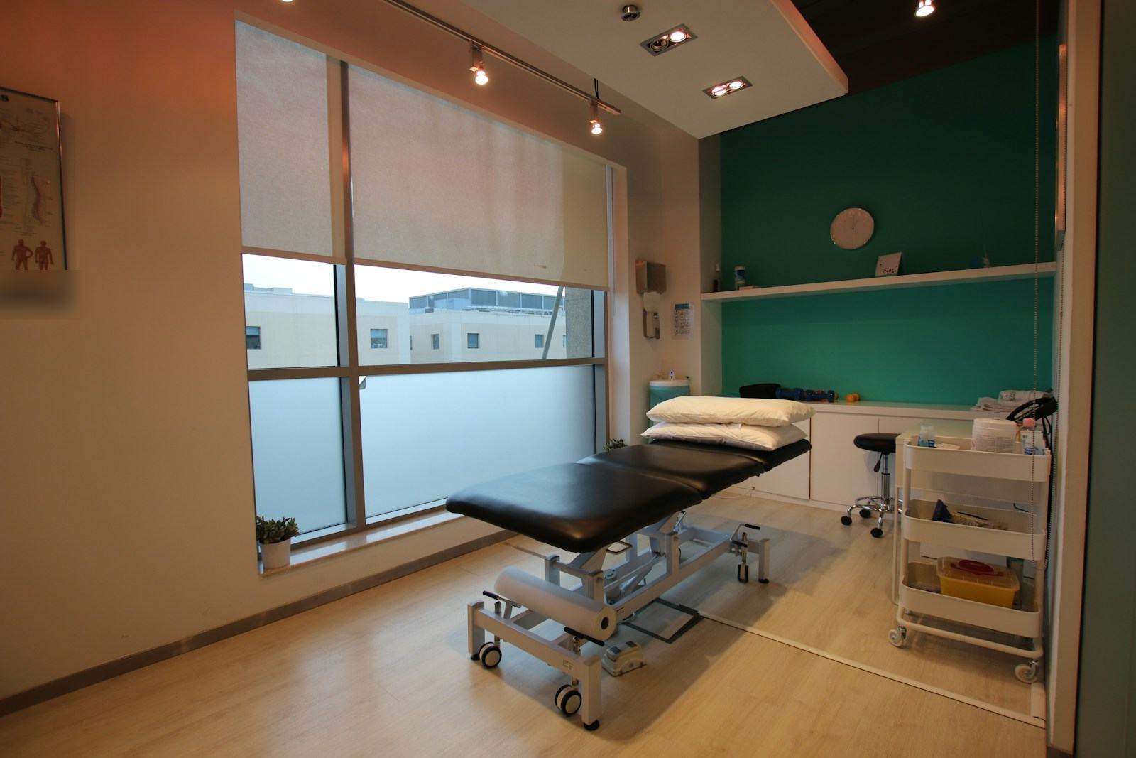 Treatment room with a padded table, a supply cart and a large window